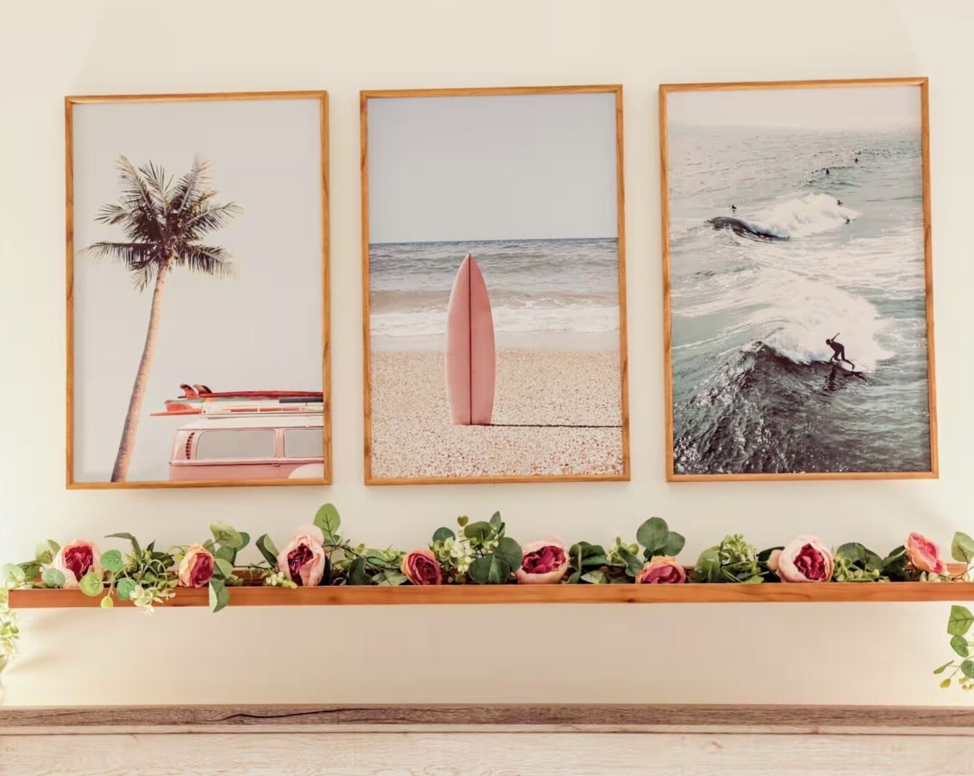 Three framed beach-themed artworks on a wall, a shelf with decorative flowers below, and a wooden shelf above.