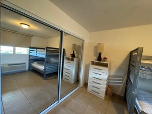 A room with a sliding door, a bed, a bedside table with a lamp, and a small cabinet. - Luxury Aguadilla Penthouse Ocean & Sunset Views 3BR (Aguadilla)