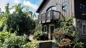 A building with a balcony, surrounded by greenery and a sign indicating a tasting room.
