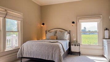 Un dormitorio con una cama, dos mesitas de noche y dos ventanas.