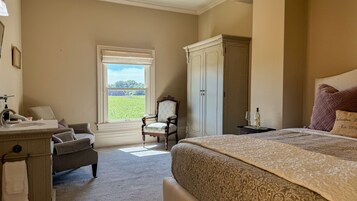 Un dormitorio con una cama grande, una silla, un armario y un ventanal con vista a un campo.