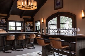 Zona de bar con barra alta, varios taburetes y una botella de vino.