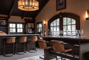 Zona de bar con barra alta, varios taburetes y una botella de vino.