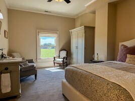 Un dormitorio con una cama grande, una silla, un armario y una ventana con vistas a un campo.
