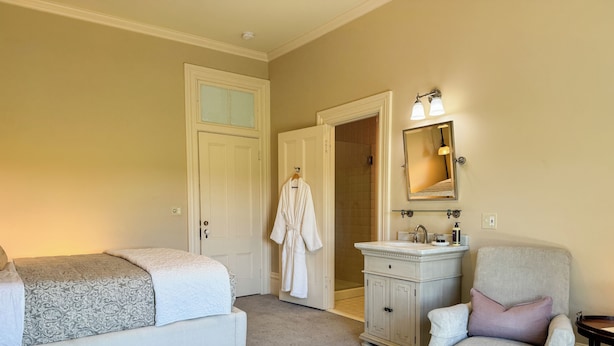 A bedroom with a bed, a chair, a vanity with a mirror, and a door leading to a bathroom.