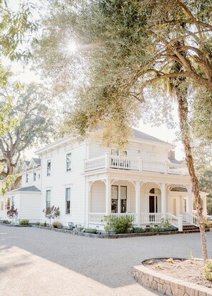 A white two-story house with a balcony, a stone retaining wall, and a driveway. - Inn at Salvestrin (St. Helena)