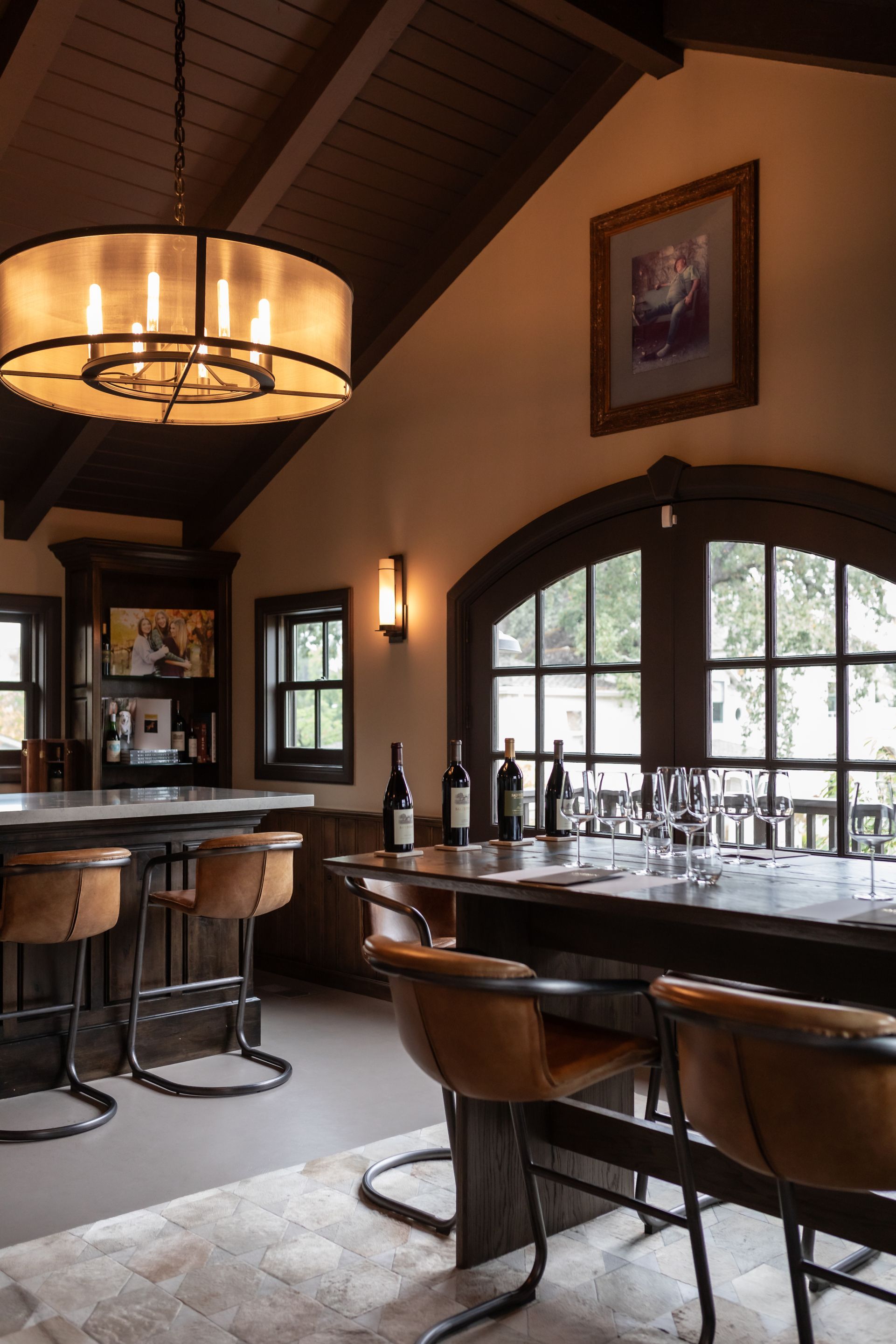 A bar area with a large wooden bar, multiple stools, and a wine bottle on the counter.