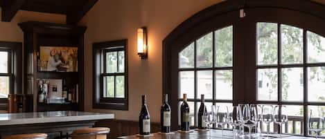 A bar area with a large wooden bar, multiple stools, and a wine bottle on the counter.