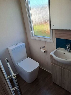 A compact bathroom with a toilet, a sink, and a window. - Cala Gran Holiday Park - Holiday Accommodation 20084 (Fleetwood)