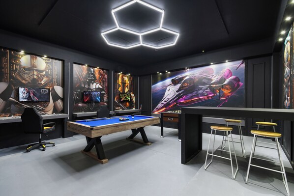Ein Spielzimmer mit Pooltisch, Gaming-Stühlen und Postern zum Thema Star Wars.
