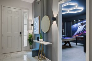 A modern room with a white door, a round mirror, a small table with a vase and plant, and a pool table. - Special Offer! Near Disney/Theater/Game Rooms/Private SPA 2425 (Kissimmee)
