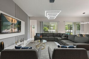 Een moderne woonkamer met een ruime hoekbank, een glazen salontafel en een schilderij aan de muur.