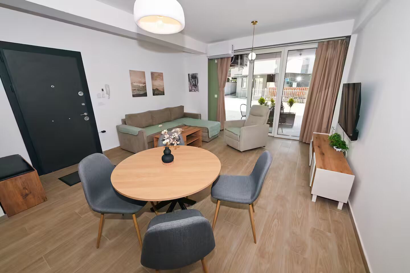 A modern living room with a round wooden table, grey upholstered chairs, a sofa, and a television.