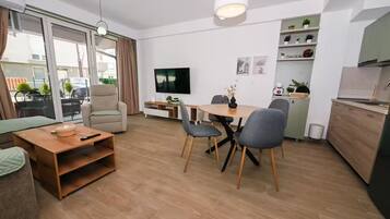A modern living room with a sofa, a coffee table, a TV, and a dining area with chairs and a table.