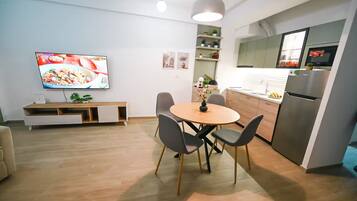 Eine moderne Küche mit Einbauofen und Kühlschrank, ein Essbereich mit rundem Tisch und Stühlen sowie ein an der Wand befestigter Flachbildfernseher.