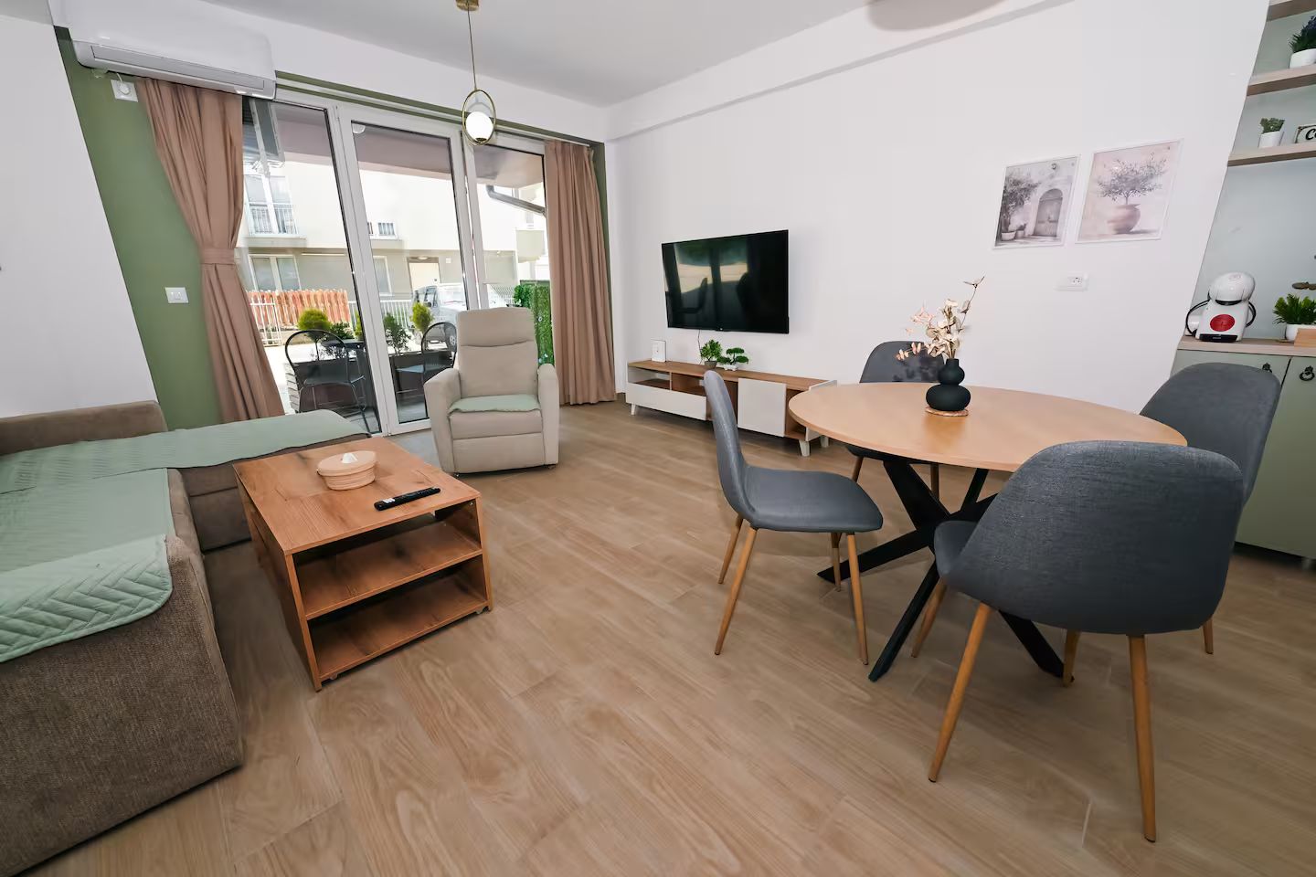 A modern living room with a sofa, a dining table with chairs, a TV, and a sliding glass door leading to an outdoor area.