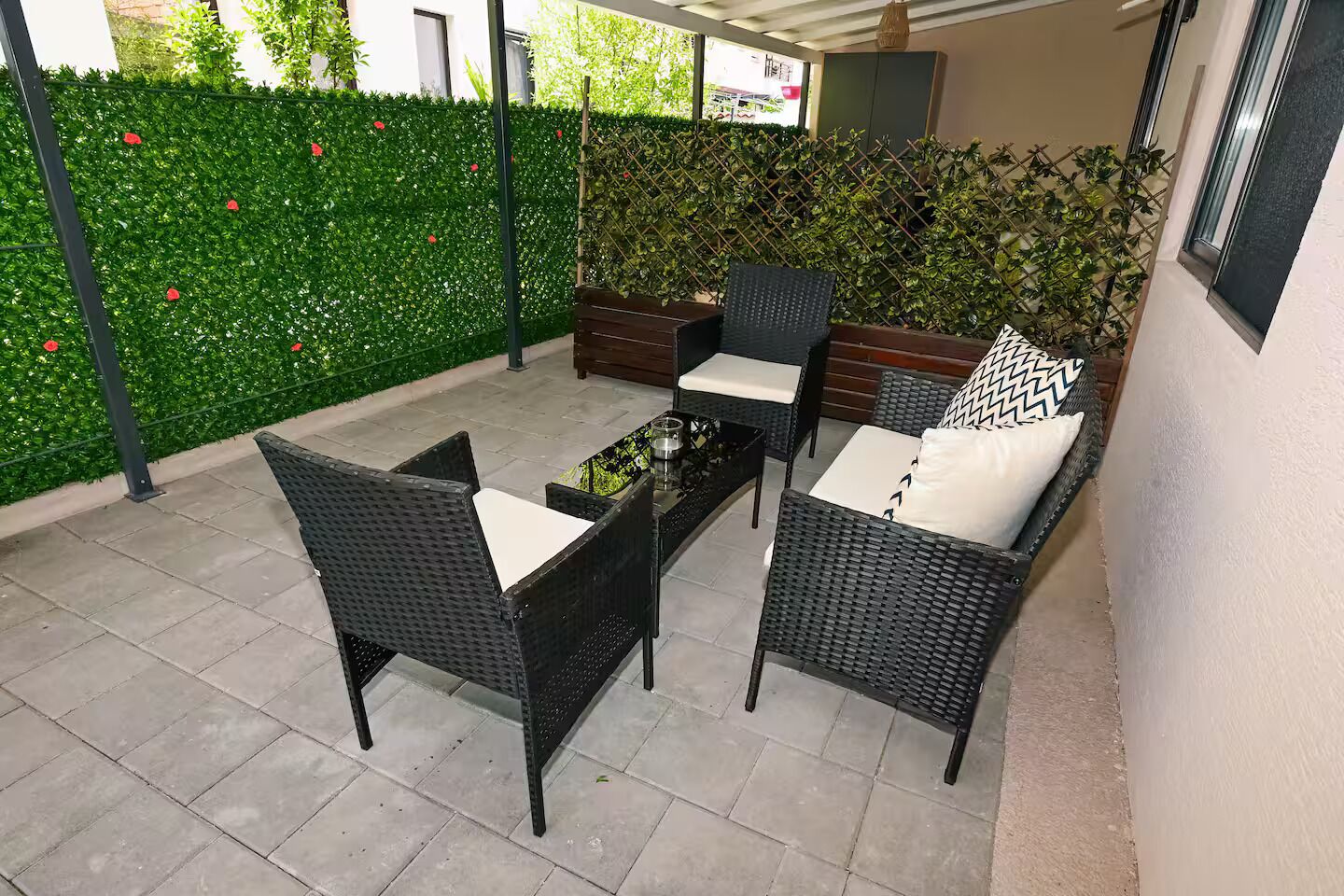 An outdoor patio area with wicker furniture, a table, and a green hedge.