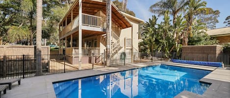A two-story building with a balcony, a swimming pool, and surrounding palm trees.