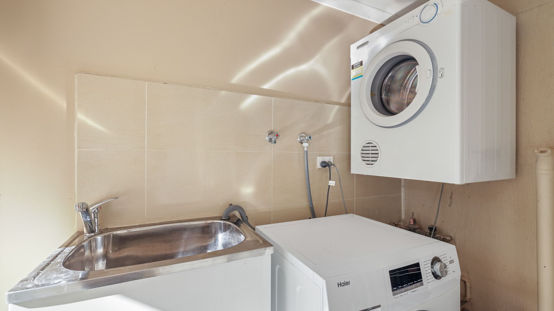 A compact laundry room with a front-loading washer and dryer, a sink, and a towel rack.