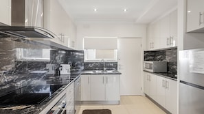 A modern kitchen with a black marble countertop, stainless steel appliances, and white cabinetry. - Unit 2 PI Holiday Retreat (Cowes)