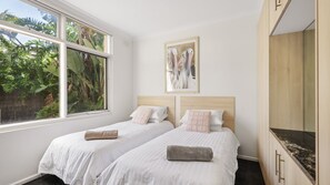 A hotel room with two beds, a large window with a view of greenery, and a painting on the wall. - Unit 2 PI Holiday Retreat (Cowes)