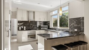 A modern kitchen with white cabinetry, a black marble countertop, stainless steel appliances, and a large window providing natural light.