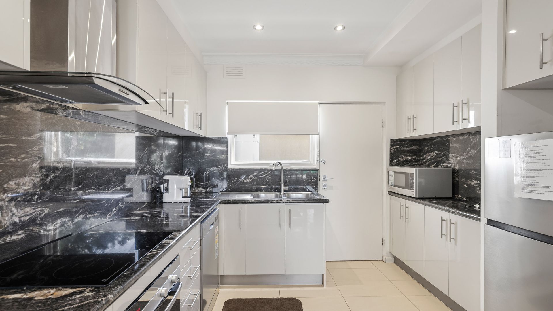 A modern kitchen with a black marble countertop, stainless steel appliances, and white cabinetry.