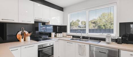 A modern kitchen with white cabinets, a black stove, a dishwasher, and a window with blinds.