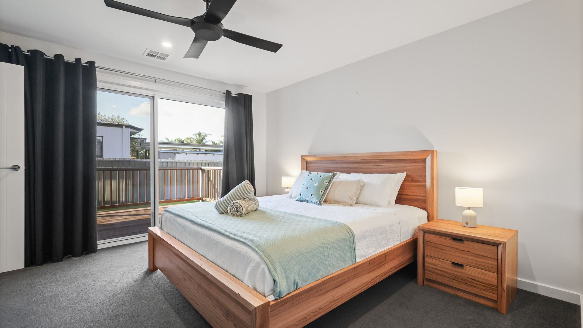 A bedroom with a wooden bed, a nightstand, a ceiling fan, and a view of the outdoors.