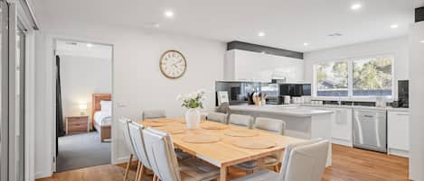 A modern kitchen with white cabinets, a central island, and a dining area with a wooden table and chairs.