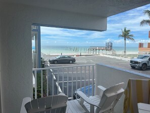 A balcony with white chairs, a view of the beach, a parking area, and a vehicle. - Condo Right on the Beach, 2-bedroom lovely Redington, Pool, Patio, Gulf Views (Redington Beach)