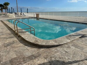 Una piscina amb barana metàl·lica, envoltada de gandules i ombrelles, amb vista a la platja.