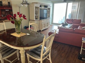 A dining area with a glass table, white chairs, and a vase of red flowers. - Condo Right on the Beach, 2-bedroom lovely Redington, Pool, Patio, Gulf Views (Redington Beach)