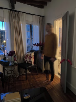 A room with a wooden floor, a table with a vase and bottle, a chair with a patterned cushion, and a door with red umbrellas. - Romantic & Comfortable Studio in Historic Burns Square with Central Air & Heat (Sarasota)