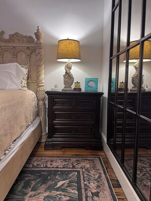 A bedroom with a bed, a nightstand with a lamp, a dresser, and a large mirror. - Romantic & Comfortable Studio in Historic Burns Square with Central Air & Heat (Sarasota)