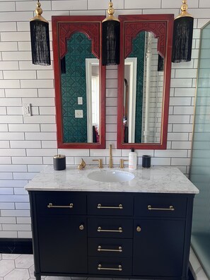 A bathroom with a white tiled wall, a black vanity with gold handles, a white sink, and two wall-mounted mirrors with decorative frames. - Romantic & Comfortable Studio in Historic Burns Square with Central Air & Heat (Sarasota)