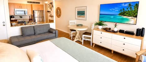 Quarto com cama, sofá, mesa de jantar, televisão e cozinha compacta.