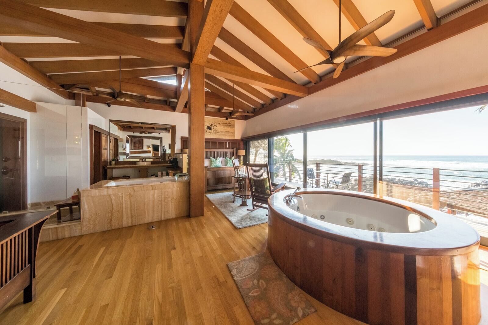Una habitación amplia con techo de madera, un ventanal con vista al océano, un jacuzzi y un comedor con vistas.