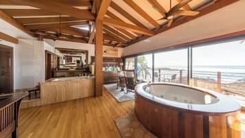 Una habitación amplia con techo de madera, un ventanal con vista al océano, un jacuzzi y un comedor con vistas.