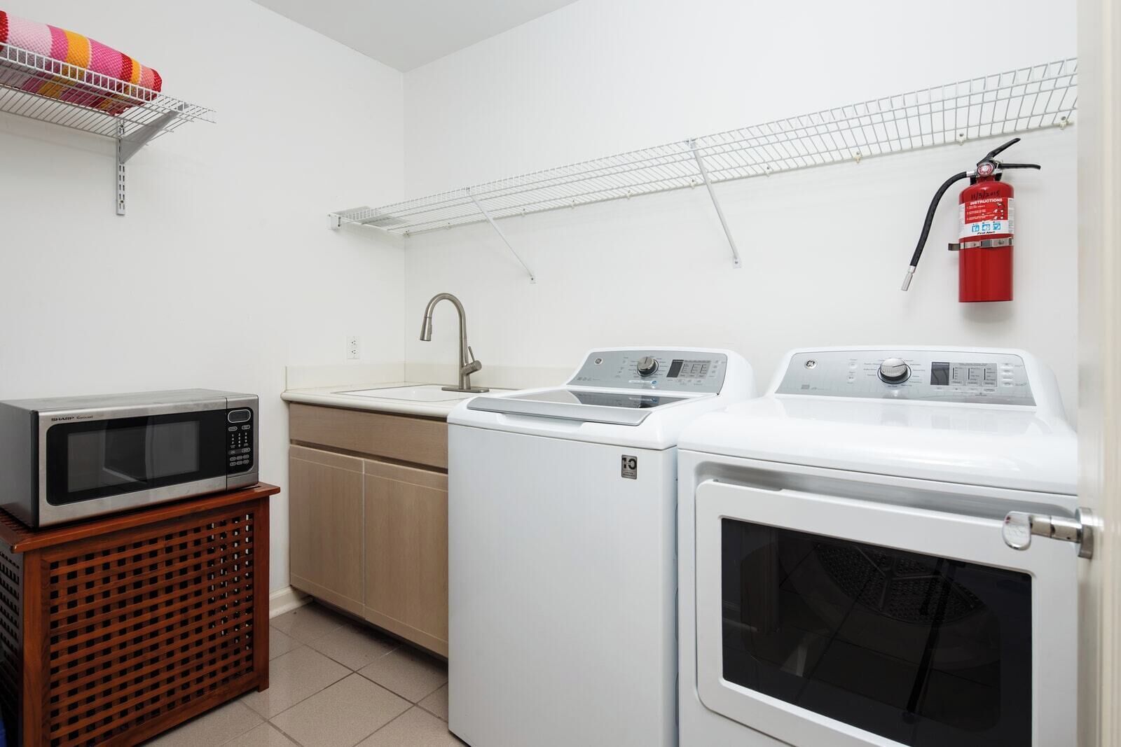 A laundry room with a microwave, sink, and stacked washer-dryer units.