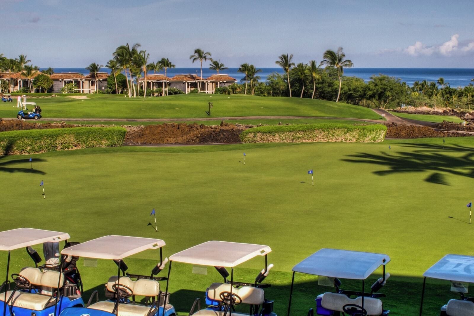 Un campo de golf con varios hoyos, un club de campo y vista al océano.