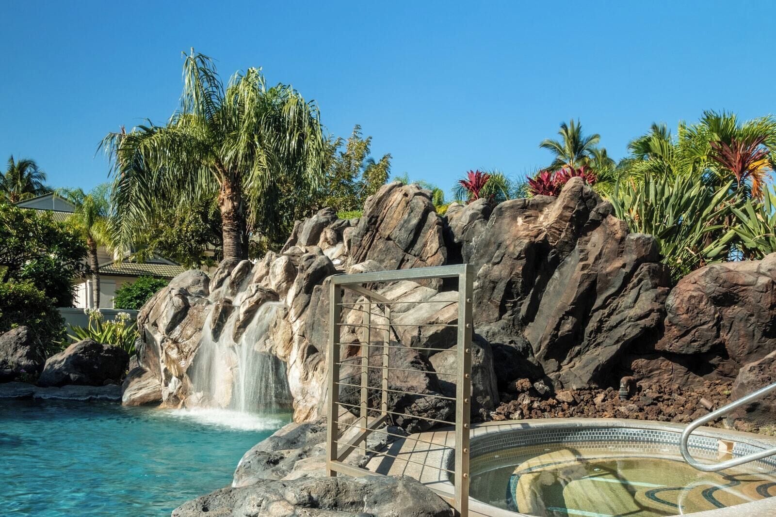 A pool area with a waterfall feature, surrounded by rocks and palm trees.