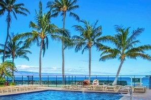 Zona de piscina con palmeras y vista al océano.
