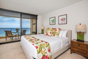 Habitación de hotel con cama, balcón con mesa y sillas, y dos cuadros en la pared.
