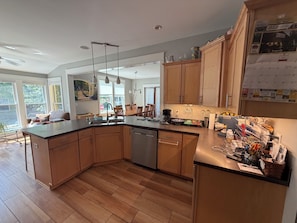 A modern kitchen with wooden cabinets, a dishwasher, and a dining area with chairs and a table.