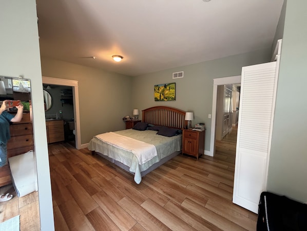 A bedroom with a bed, bedside tables, a nightstand, a mirror, a door, and a hallway leading to another room.