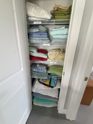 A closet with shelves labeled 'QUEEN,' 'TWIN,' and 'KING,' containing folded clothes.