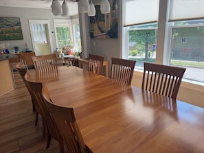 A dining area with a wooden table and chairs, large windows with a view, and a painting on the wall.