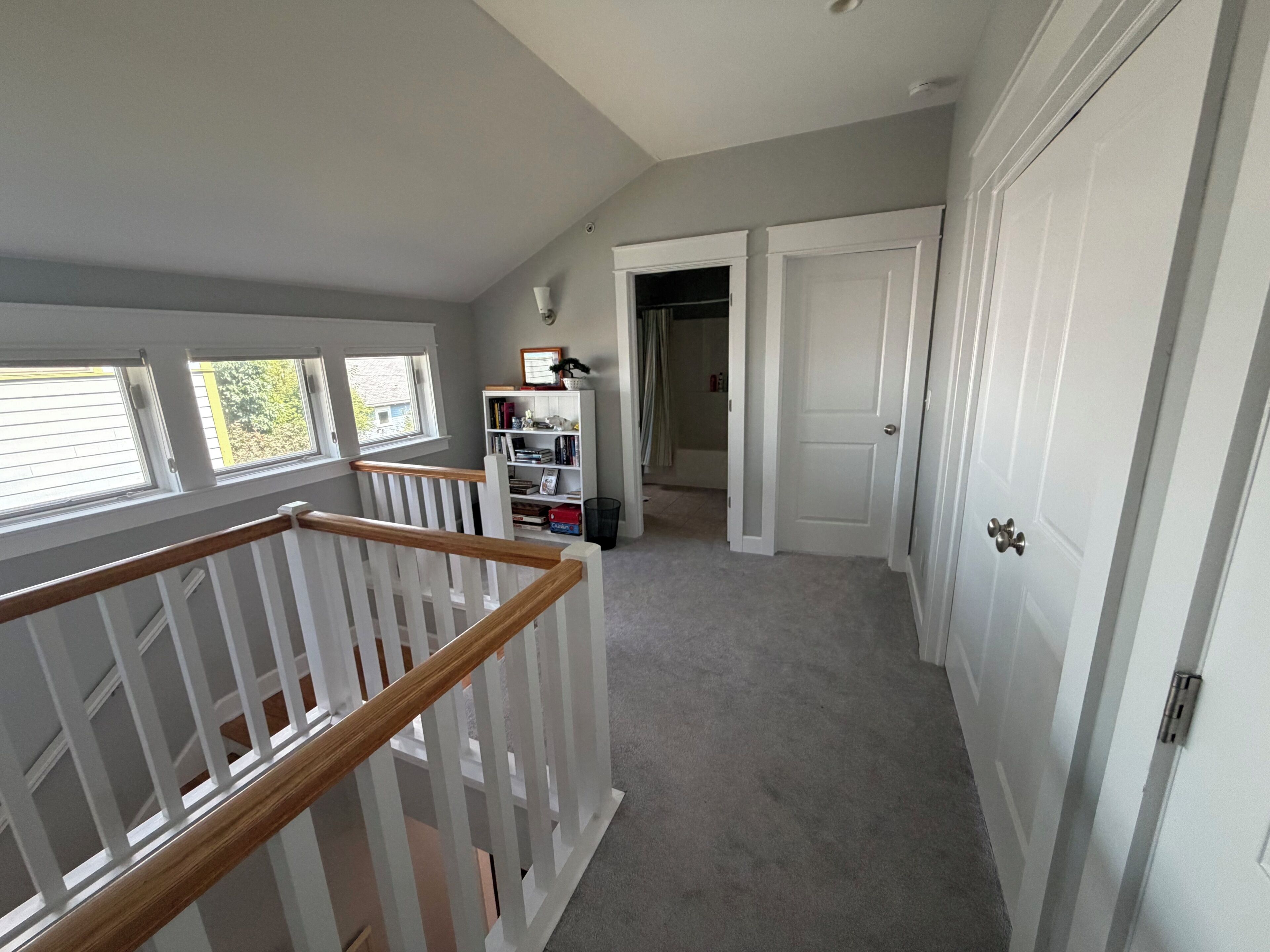 A hallway with a staircase, a bookshelf, and a door leading to another room.