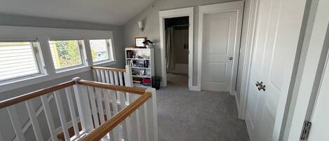 A hallway with a staircase, a bookshelf, and a door leading to another room.